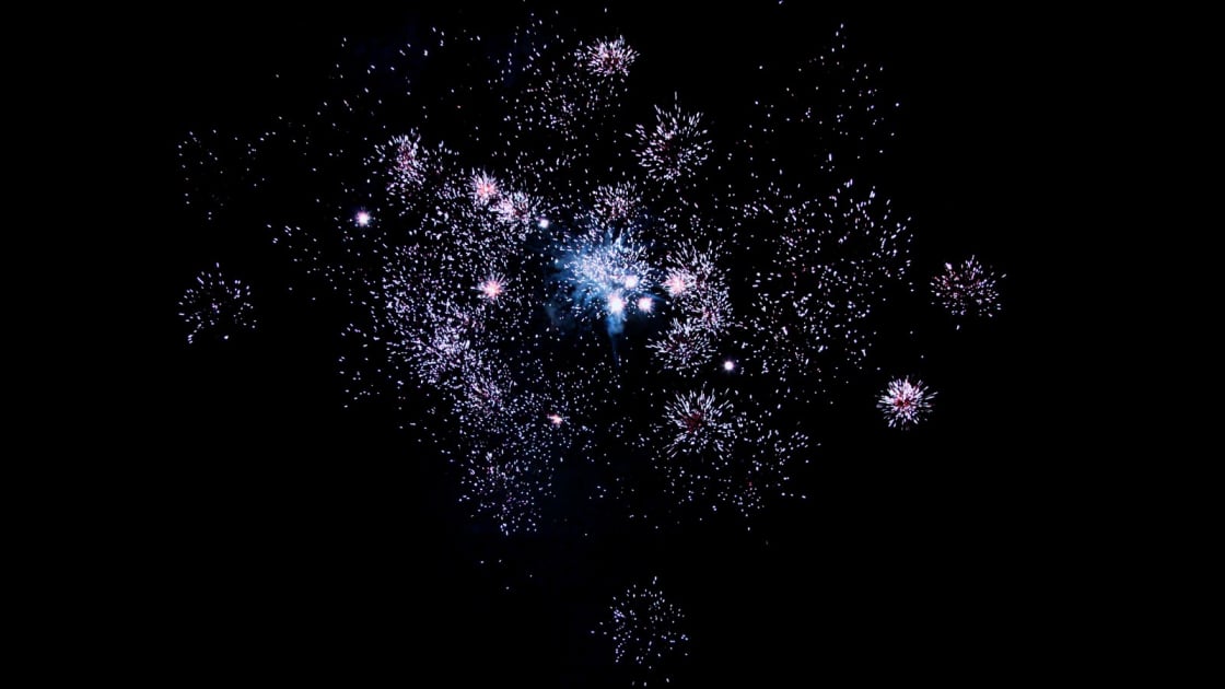 Pale violet firework bursts scatter sparks across a black night sky during a Fourth of July show in Utah