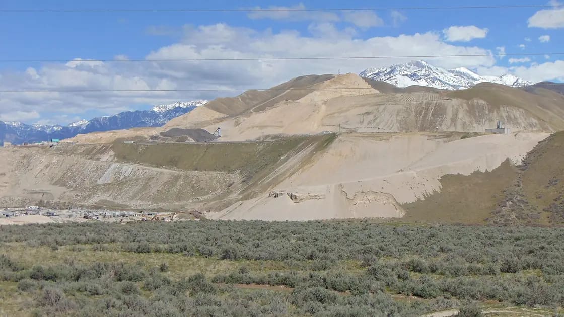 Sagebrush in the foreground below the excavated slopes of the gravel pits on the Traverse Mountains, with snow-capped peaks behind