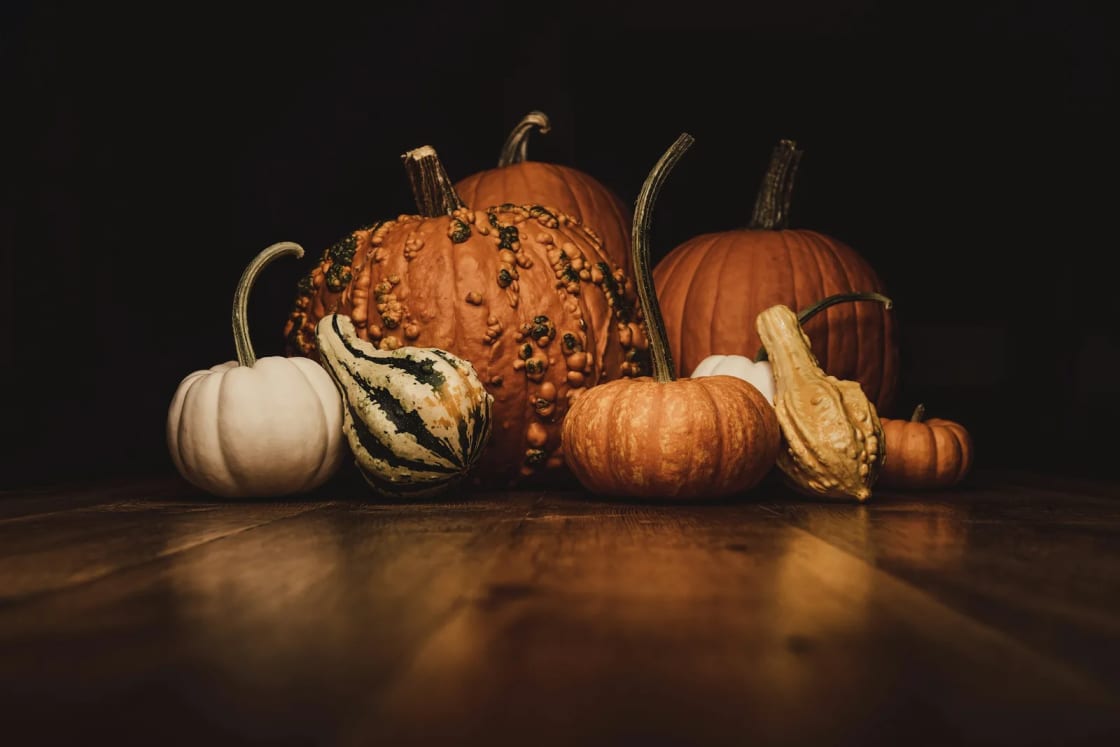 Orange and white pumpkins and striped gourds grouped on a dark wood table in low light, a ready-made fall centerpiece.