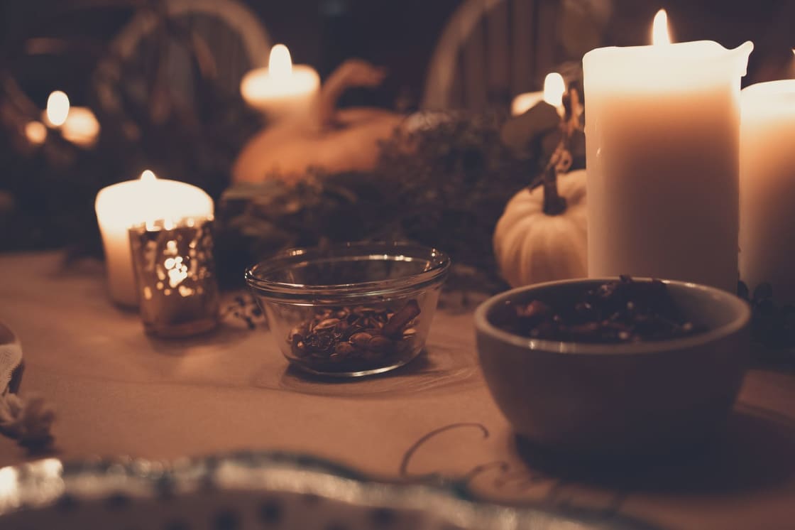 A candlelit autumn table with pillar candles, small pumpkins and bowls of nuts and spices