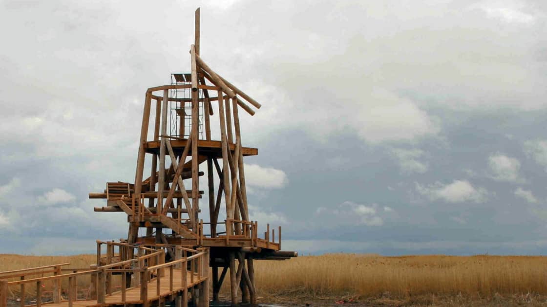 The log-framed observation tower and railed boardwalk at the Great Salt Lake Shorelands Preserve, with golden reeds stretching to the horizon under heavy gray clouds