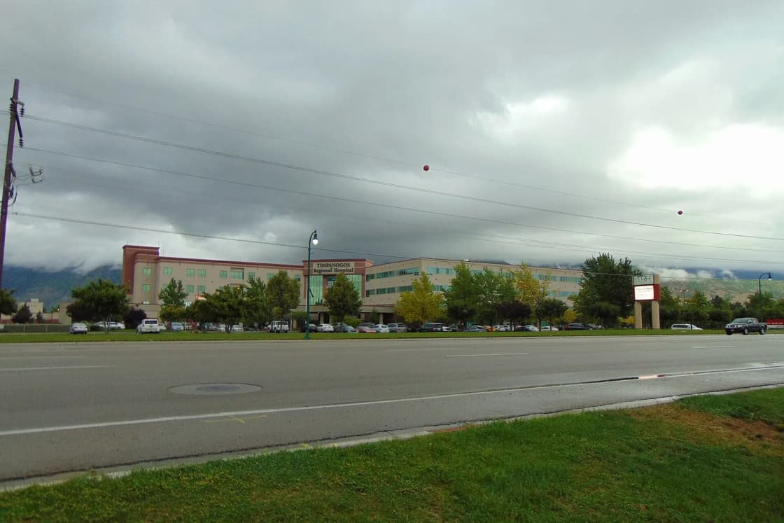 Timpanogos Regional Hospital in Orem seen across a wide road under heavy gray clouds.