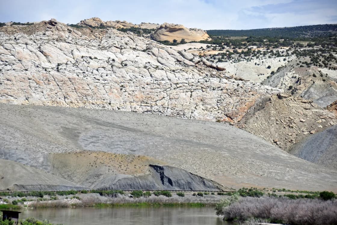 Pale sandstone cliffs and gray shale slopes rise above a quiet river in Dinosaur National Monument.