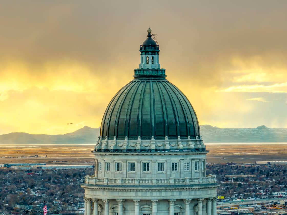 The green copper dome of the Utah State Capitol rising above Salt Lake City at sunset, with the valley and distant mountains behind it