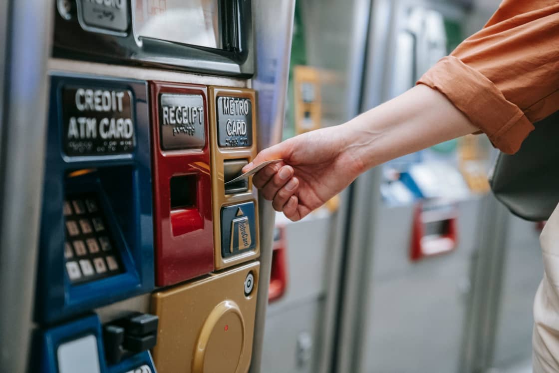 A hand inserting a payment card into a transit ticket vending machine labeled for credit cards, receipts and metro cards
