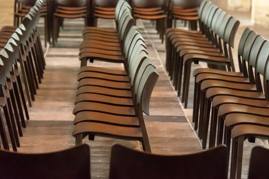 Rows of empty wooden folding chairs set out in aisles on a bare floor before a meeting