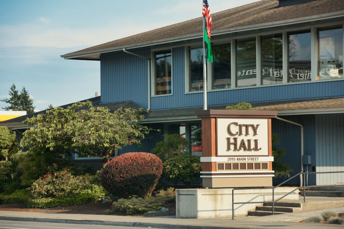A low blue-gray municipal building with a large CITY HALL sign at the entrance and an American flag flying on a pole beside it