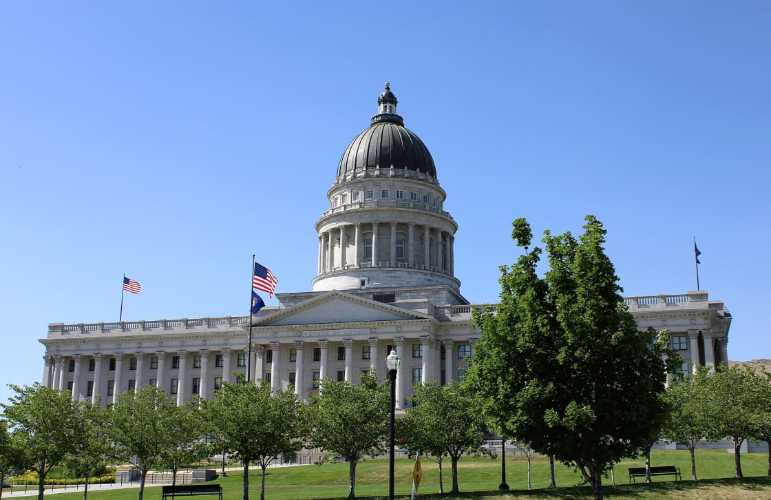 The Utah State Capitol in Salt Lake City, its granite colonnade and dome seen from the lawn beneath a clear sky