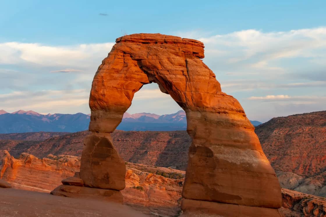 Delicate Arch in Arches National Park glowing orange in evening light, the La Sal Mountains on the horizon behind it
