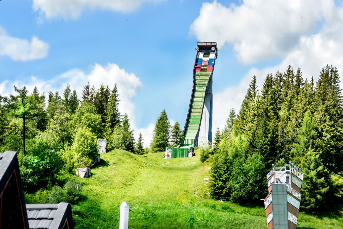 A steep ski jump ramp on a green summer hillside under a blue sky