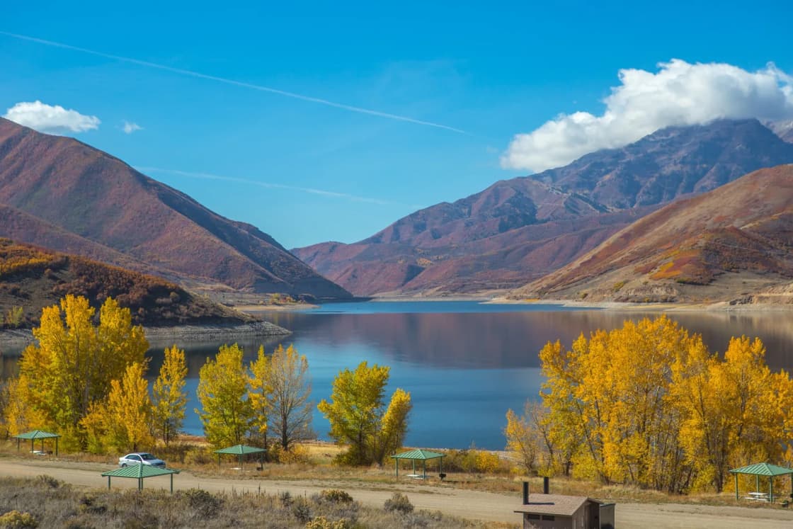 Golden fall trees and picnic shelters line the shore of Deer Creek Reservoir below red-brown mountains.