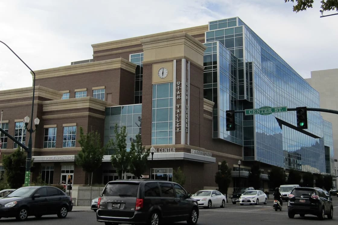 The brick and blue glass Utah Valley Convention Center on Center Street in downtown Provo, with cars at the intersection.