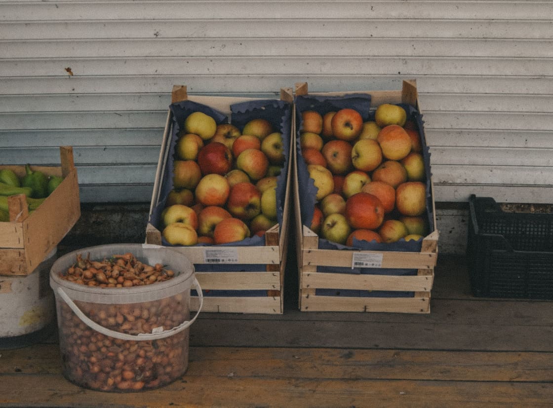 Wooden crates of apples and a bucket of onions at an outdoor market stall