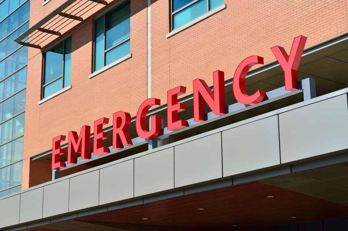 Large red EMERGENCY letters mounted above a hospital entrance on a brick and glass exterior