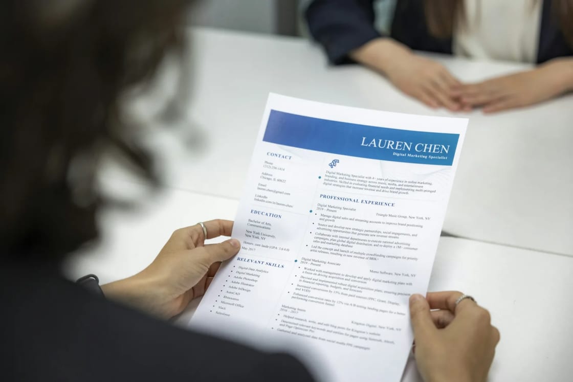A recruiter holding up a printed one-page resume across the table from a job candidate