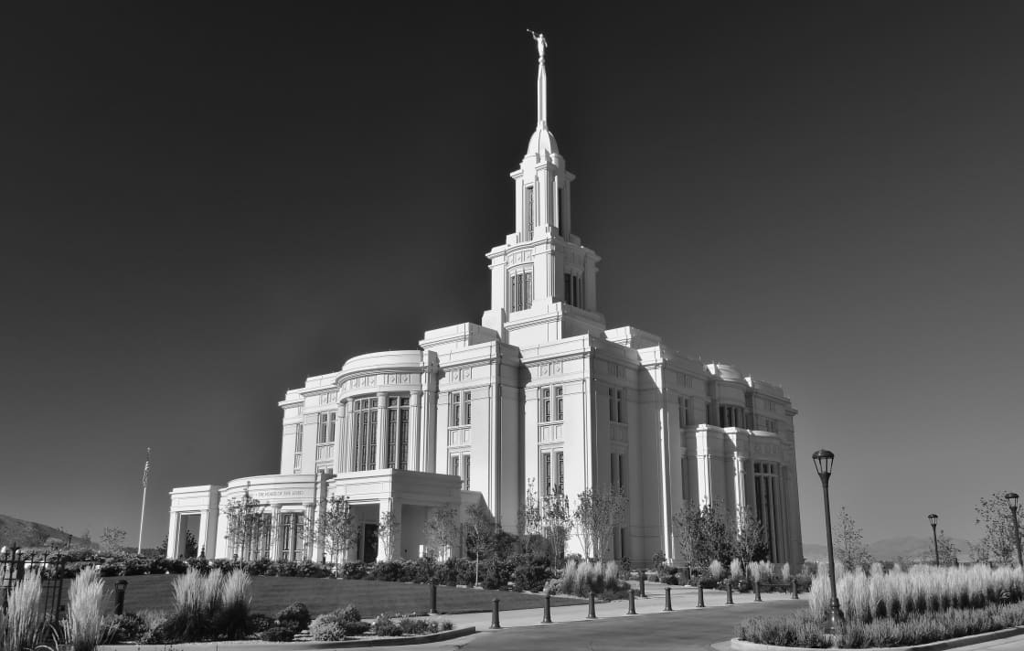 A white stone temple with a tall central spire lit by low sunrise light, set behind landscaped grounds and a bare tree