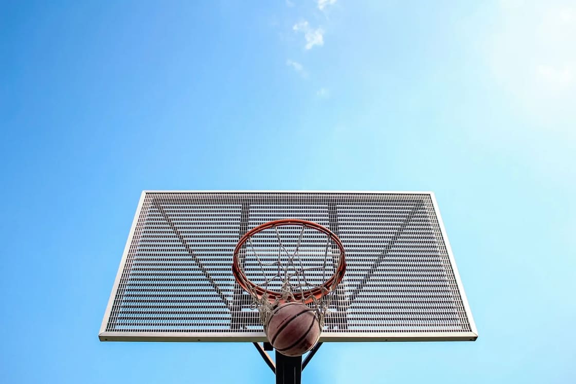 A basketball dropping through an outdoor hoop, seen from below against a blue sky