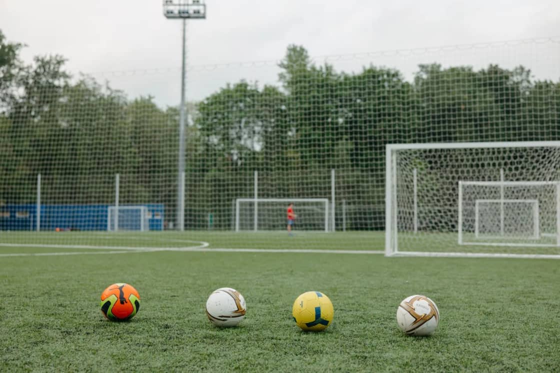 Four soccer balls lined up on artificial turf in front of an empty goal