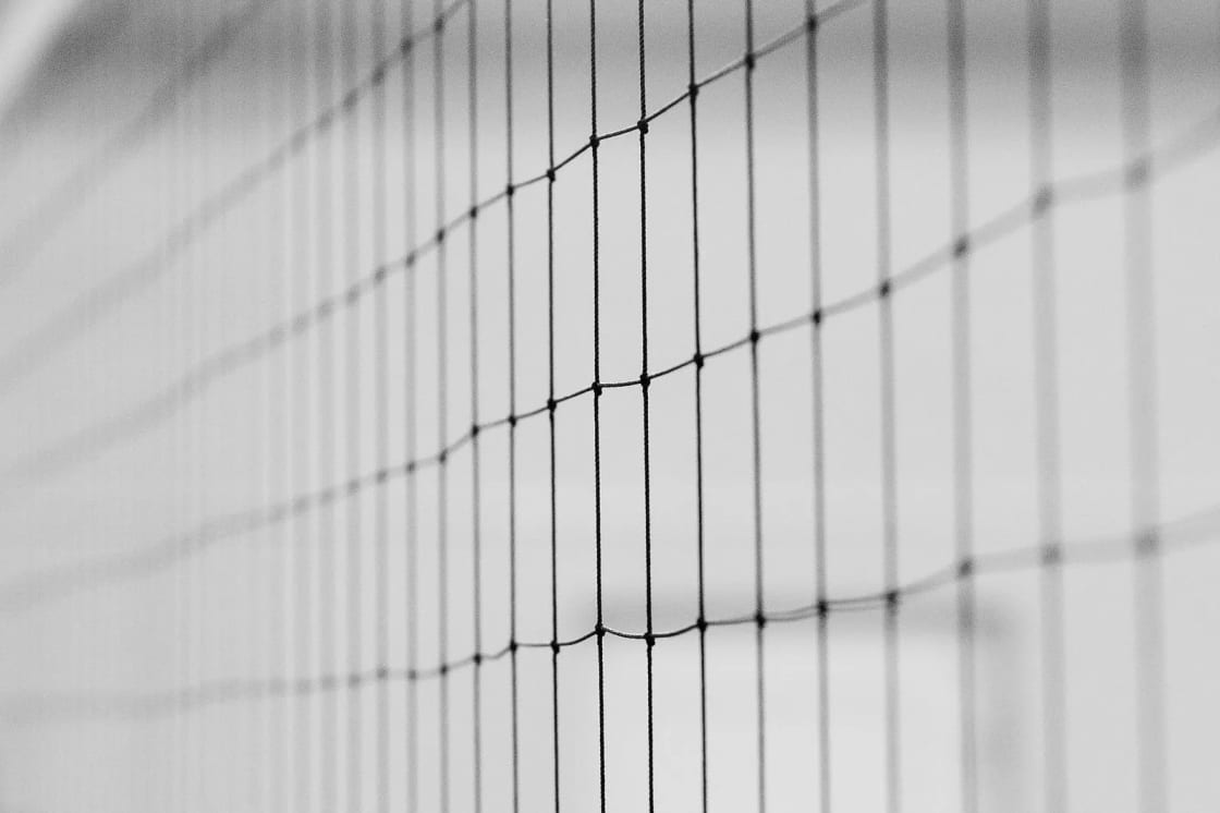 Close-up of an indoor volleyball net in black and white, with the gym blurred behind it