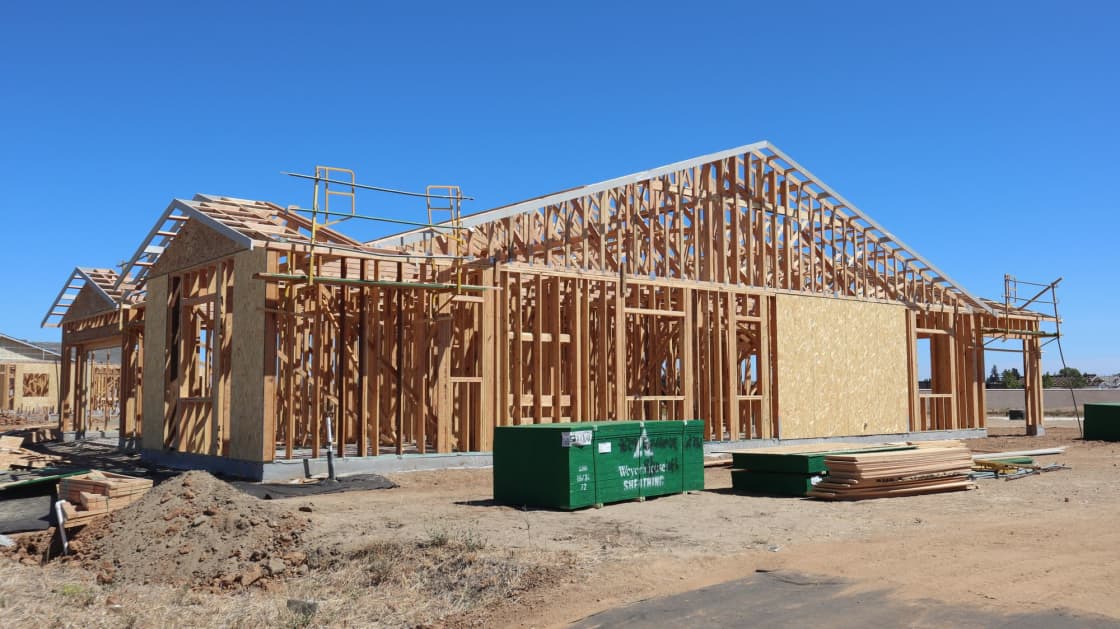 A house at the timber-framing stage on a cleared lot under a clear sky