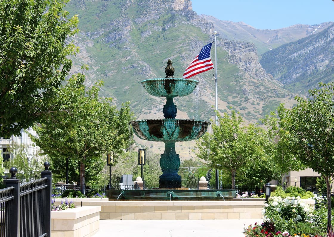 A two-tier bronze fountain on a landscaped downtown block, with the Wasatch Range rising behind it