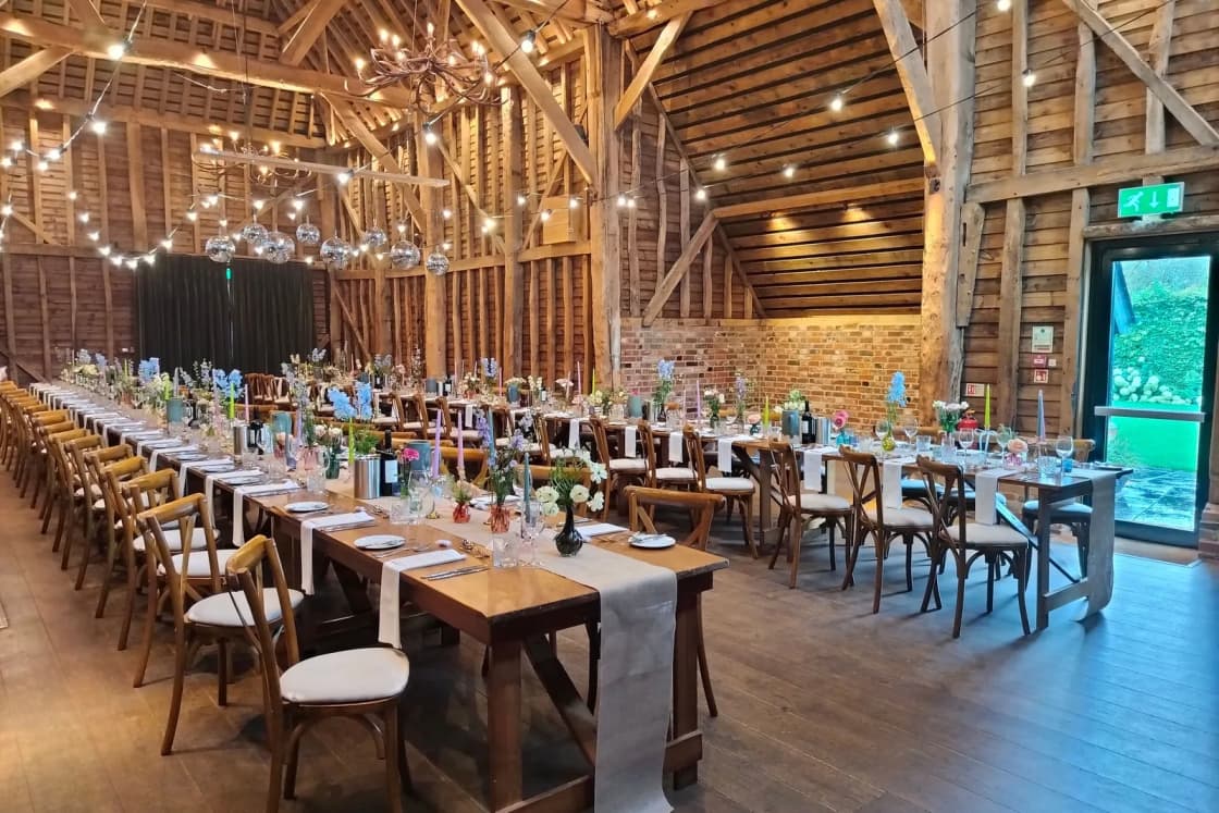 Long reception tables under strings of lights inside a large wooden barn.