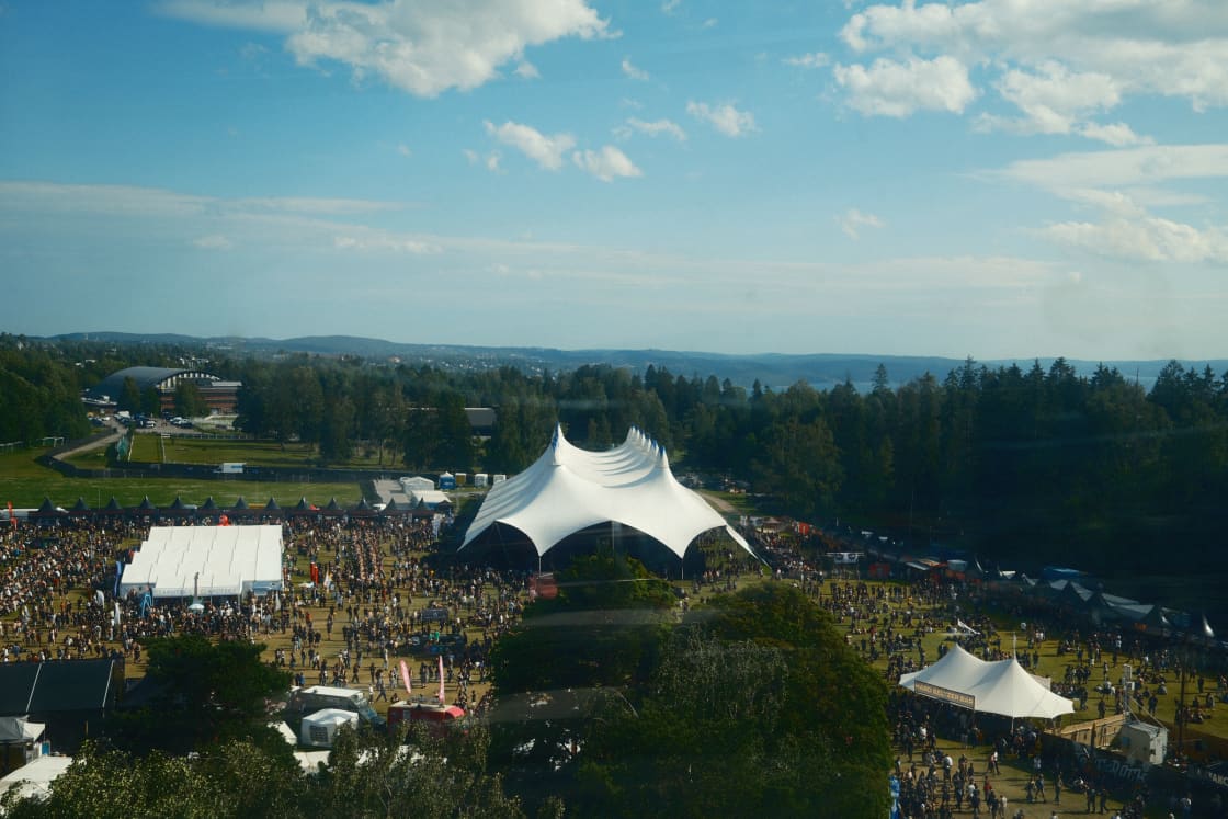 An aerial view of an outdoor festival with white peaked tents and a crowd on a green field