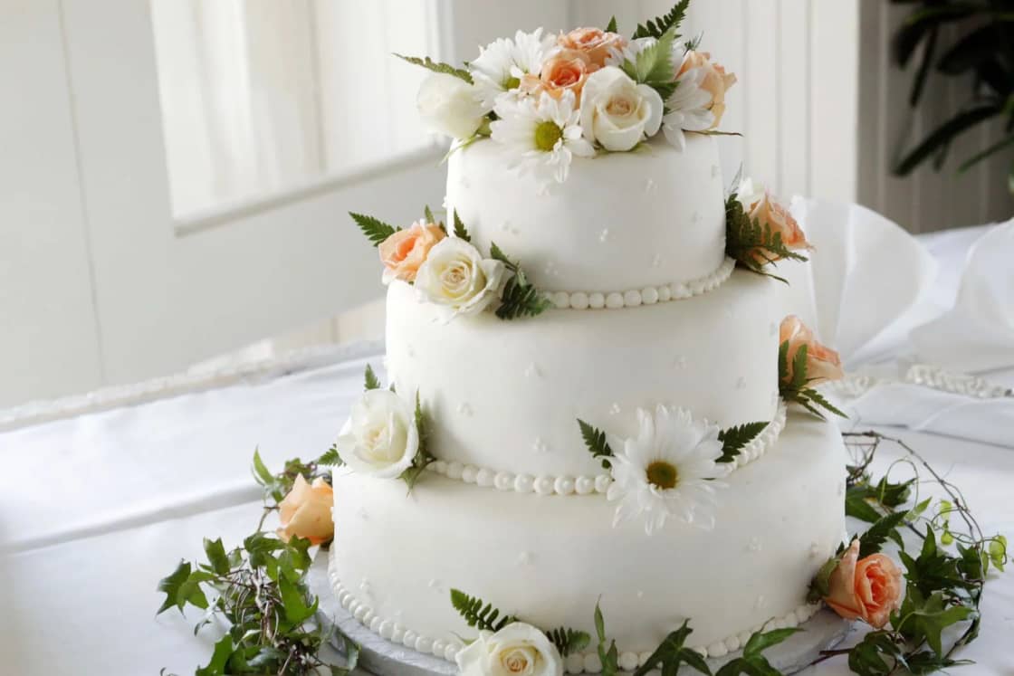 A three-tier white wedding cake decorated with orange and white flowers.
