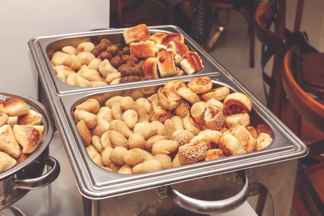 Silver chafing dishes filled with baked pastries on a catering buffet.