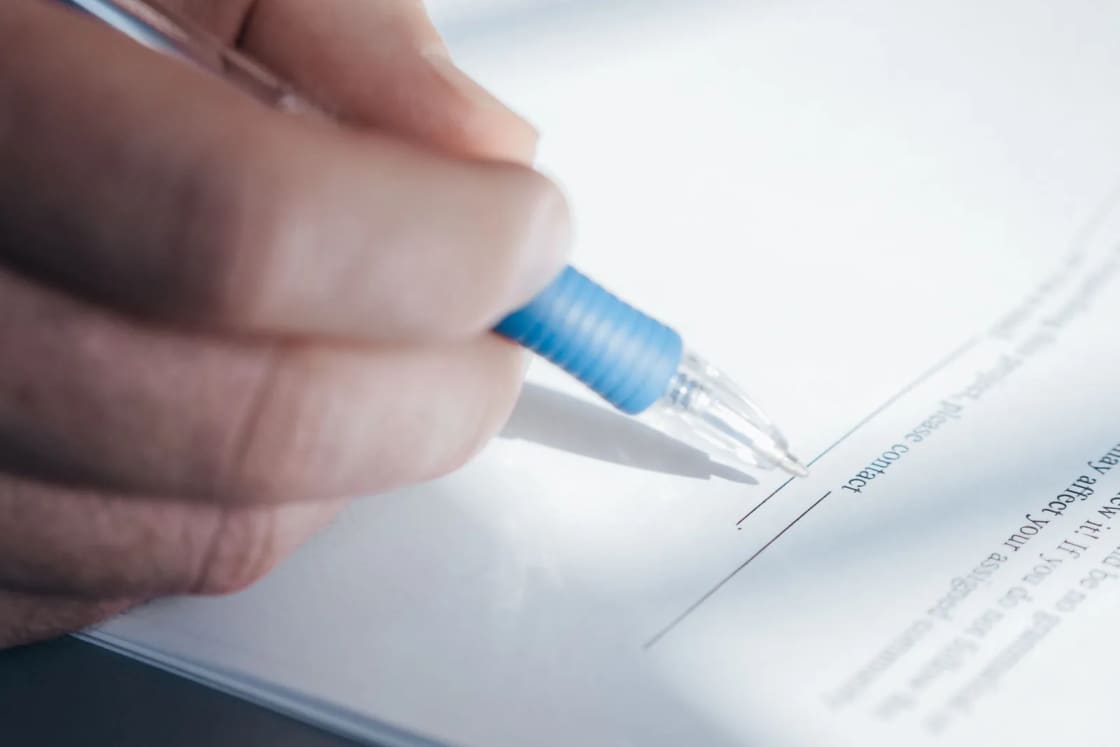 A hand signing a printed document with a blue pen.