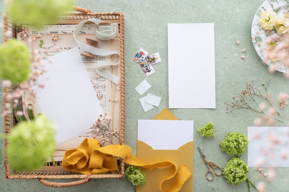 Flat lay of blank wedding stationery with a gold envelope, ribbon, scissors and dried flowers