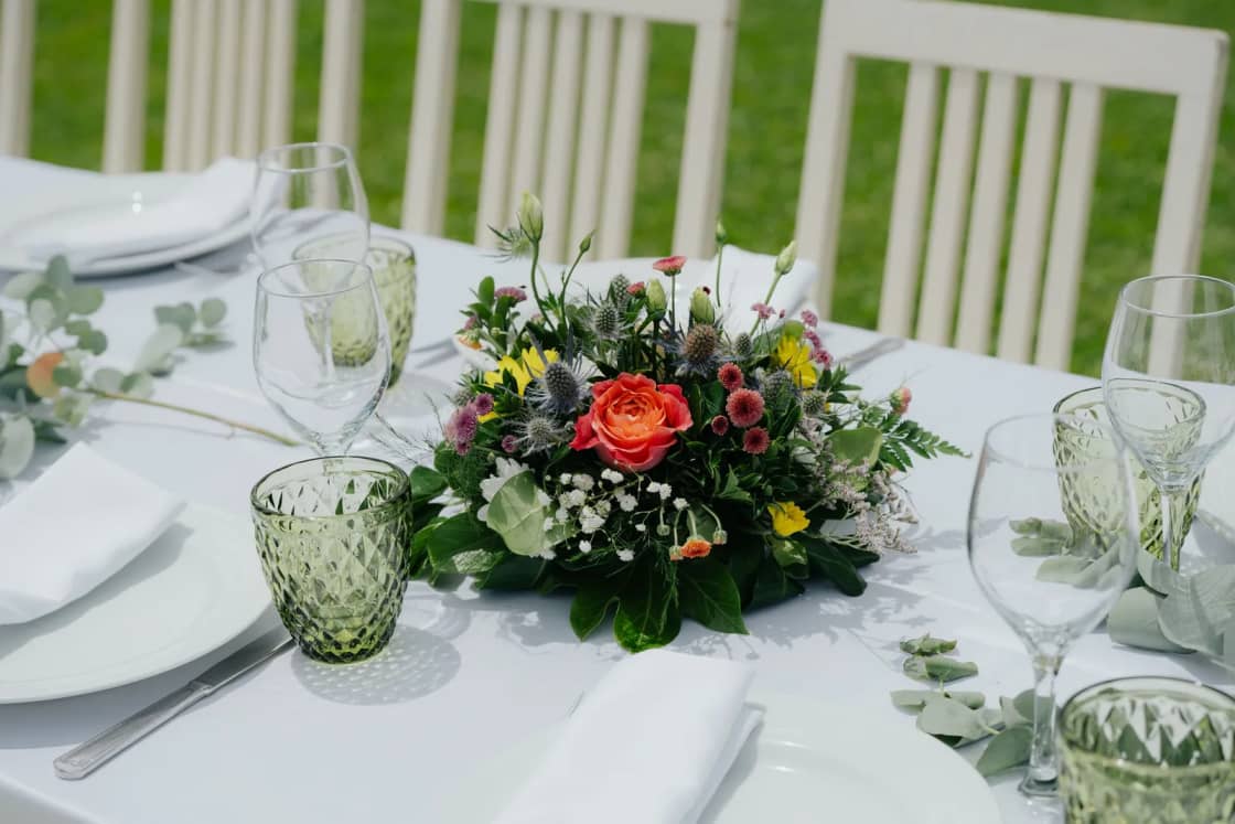 A daytime table set with white plates, green glasses and a centerpiece of mixed flowers.