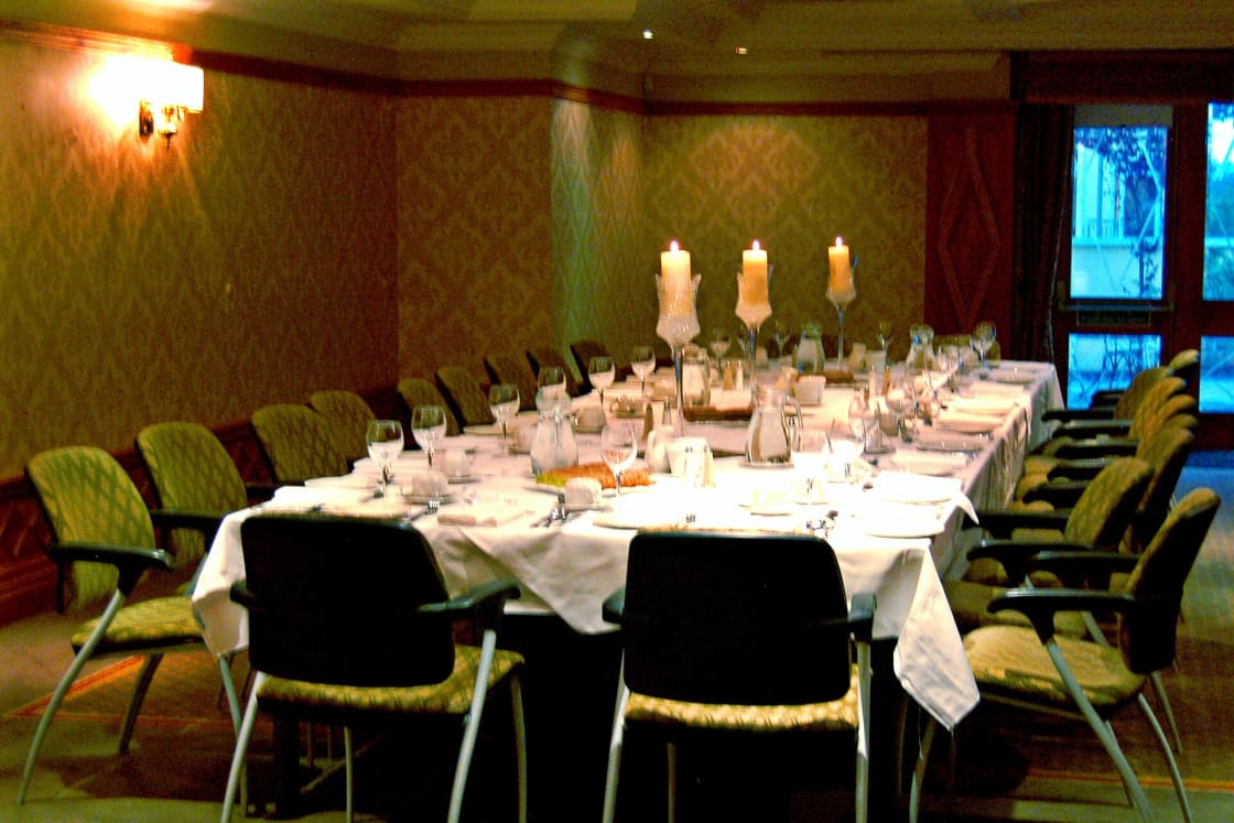 A long banquet table set with white linen, lit candles and place settings in a private dining room