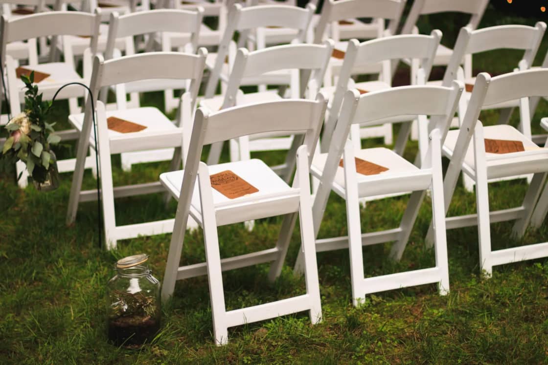Rows of white folding chairs set on a lawn for an outdoor ceremony.