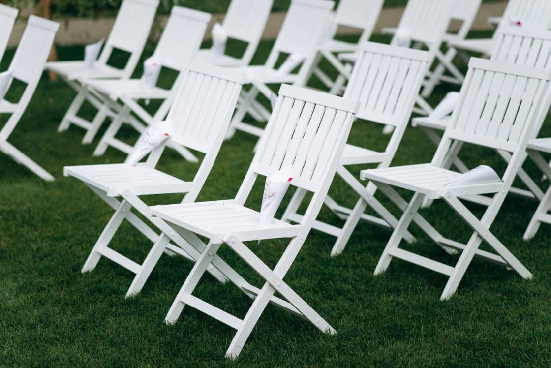 Rows of white wooden folding chairs set up on grass for an outdoor ceremony