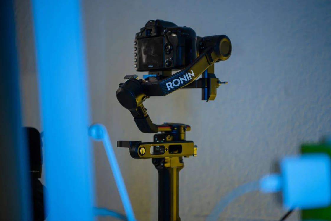 A video camera mounted on a handheld gimbal stabilizer against a blue wall.