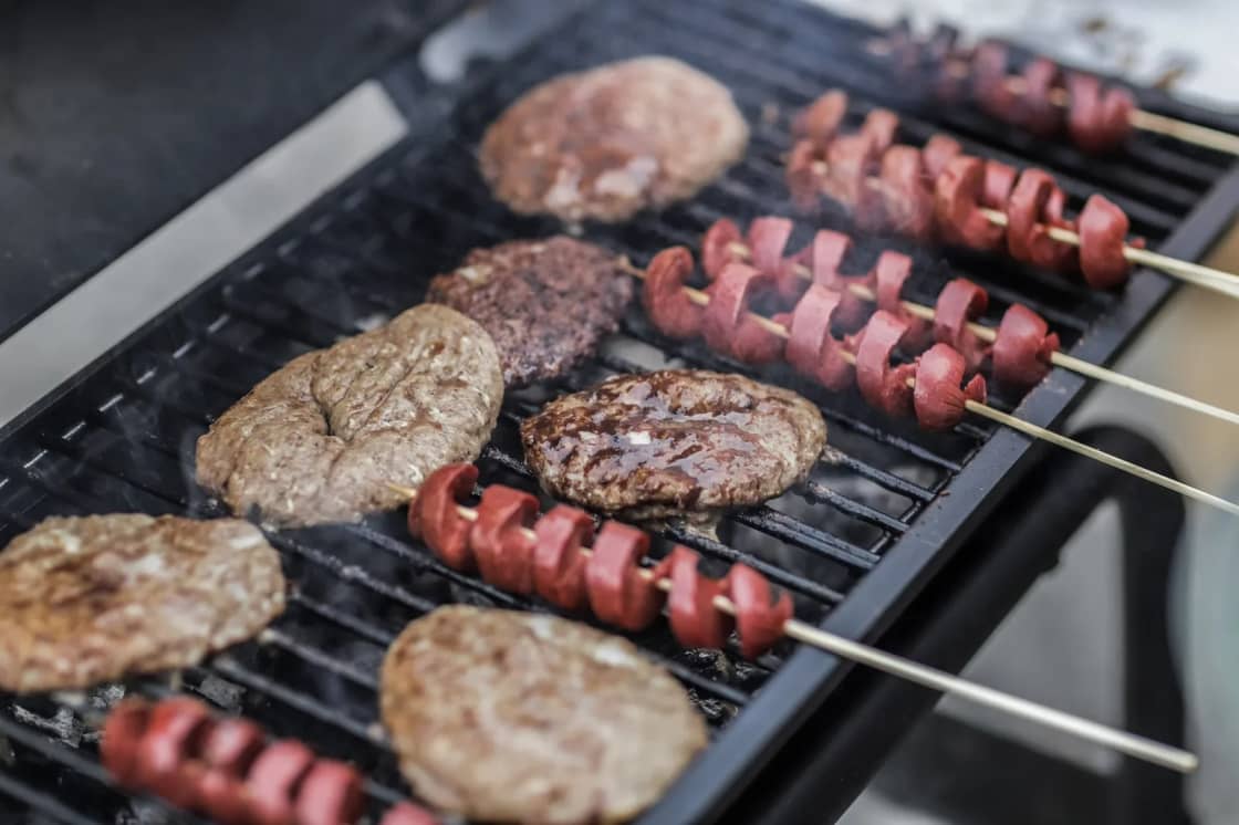 Burgers and sausage skewers cooking on a grill