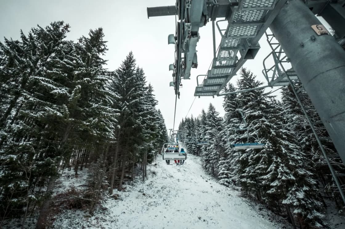 A chairlift line runs up a snow-covered slope between rows of frosted evergreens under a gray winter sky — working a ski season at a Utah resort