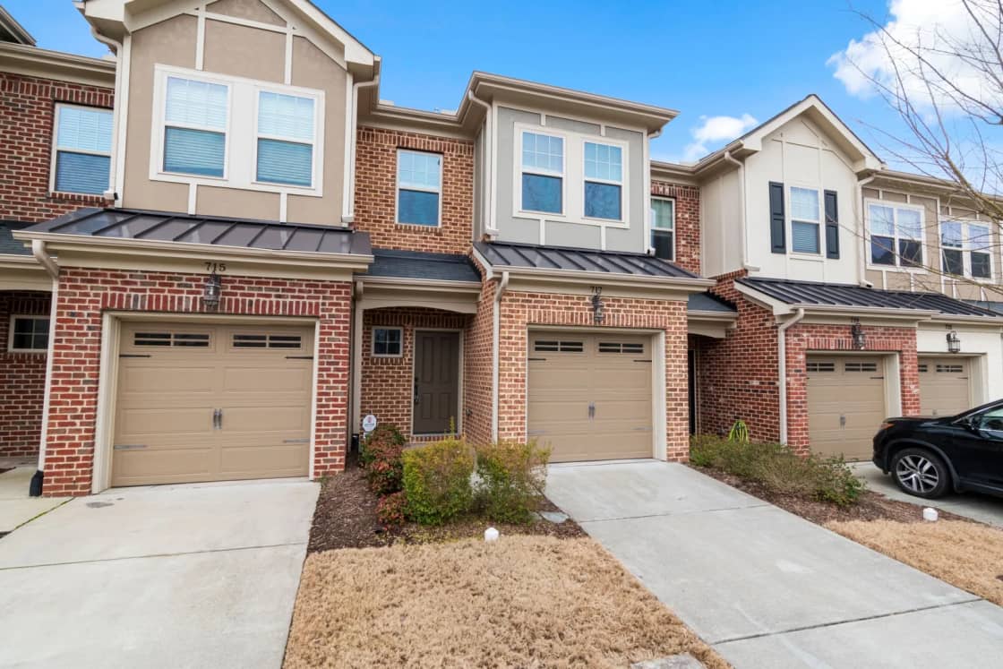 Brick and siding townhomes with tan garage doors and short driveways under a blue sky.