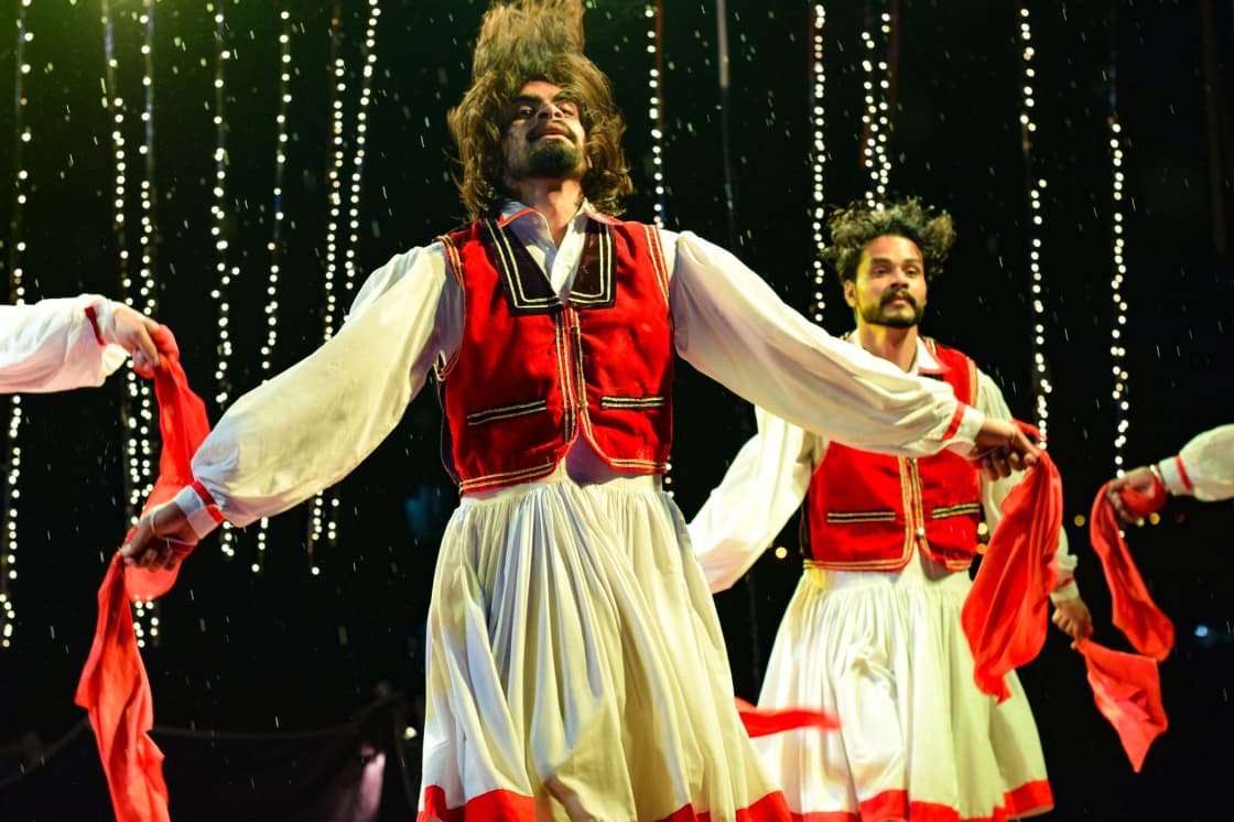 Dancers in red and white traditional costume performing on stage in front of hanging lights