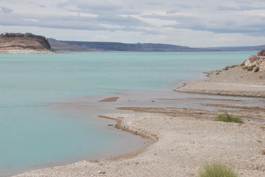 A calm turquoise reservoir with a pale gravel shoreline and low desert bluffs beyond.