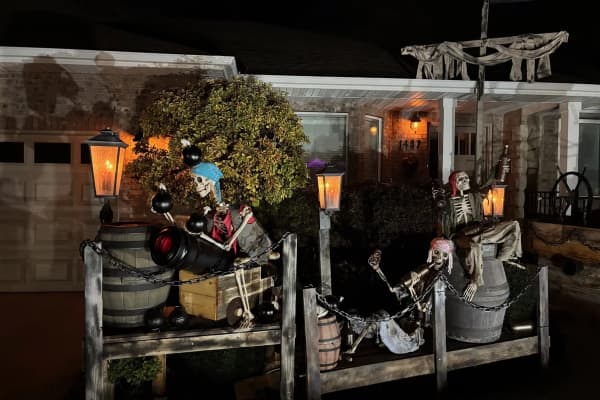 Skeleton pirates on the front porch at night with a cannon, cannonballs, barrels and glowing lanterns behind a chain railing