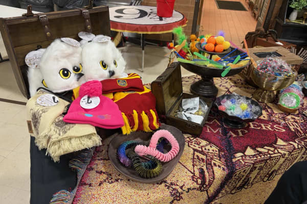 Breakfast Games prizes on a Marauder's Map blanket: two white Hedwig owl hats, a pink beanie, a red and gold scarf, 3-D printed articulated snakes in a wooden bowl, and bowls of small toys and fidget spinners