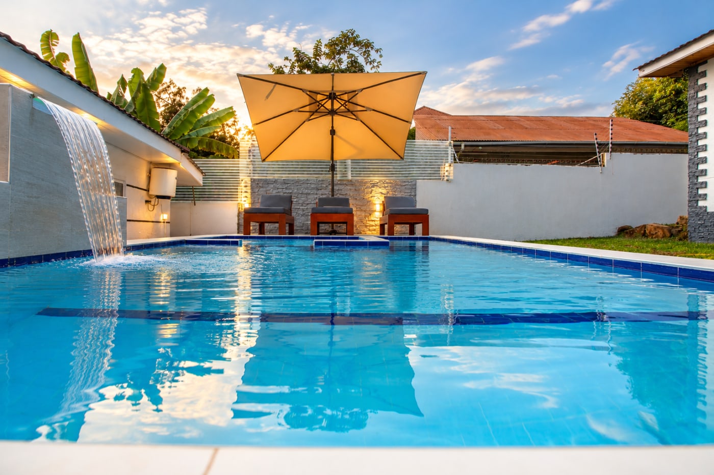 The pool by day, with a waterfall, umbrella and loungers