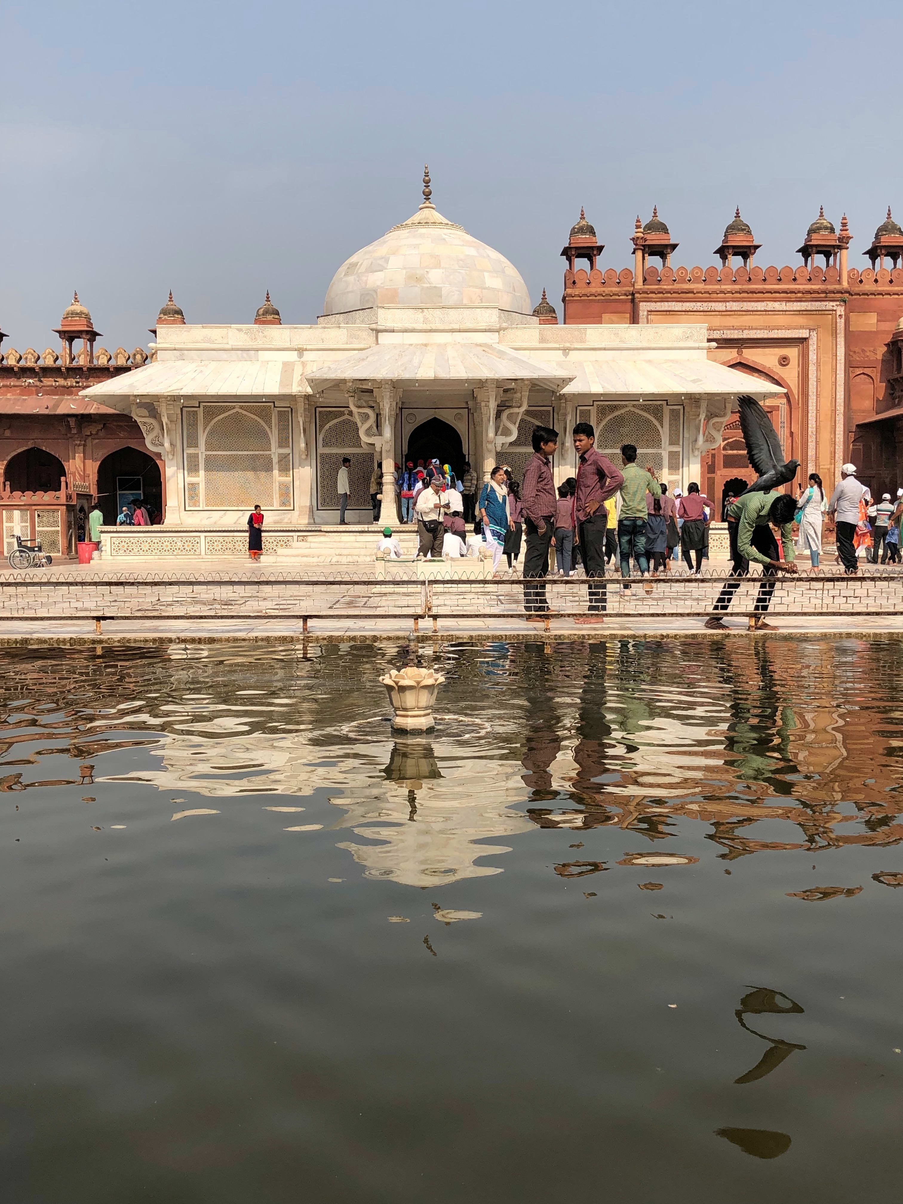 Visitors beside the white marble tomb of Salim Chishti, with reflections in the foreground.