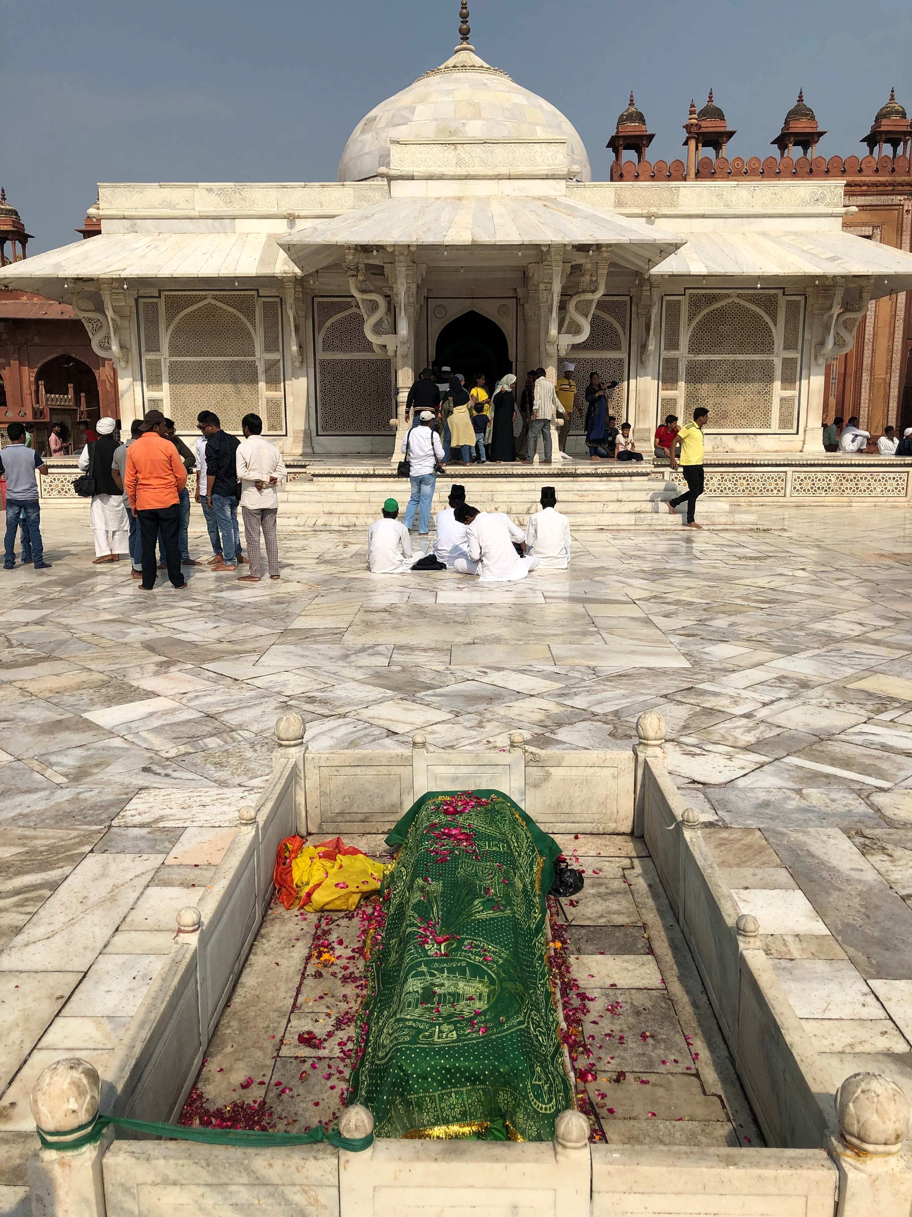 A foreground grave and visitors beside the white marble tomb of Salim Chishti.