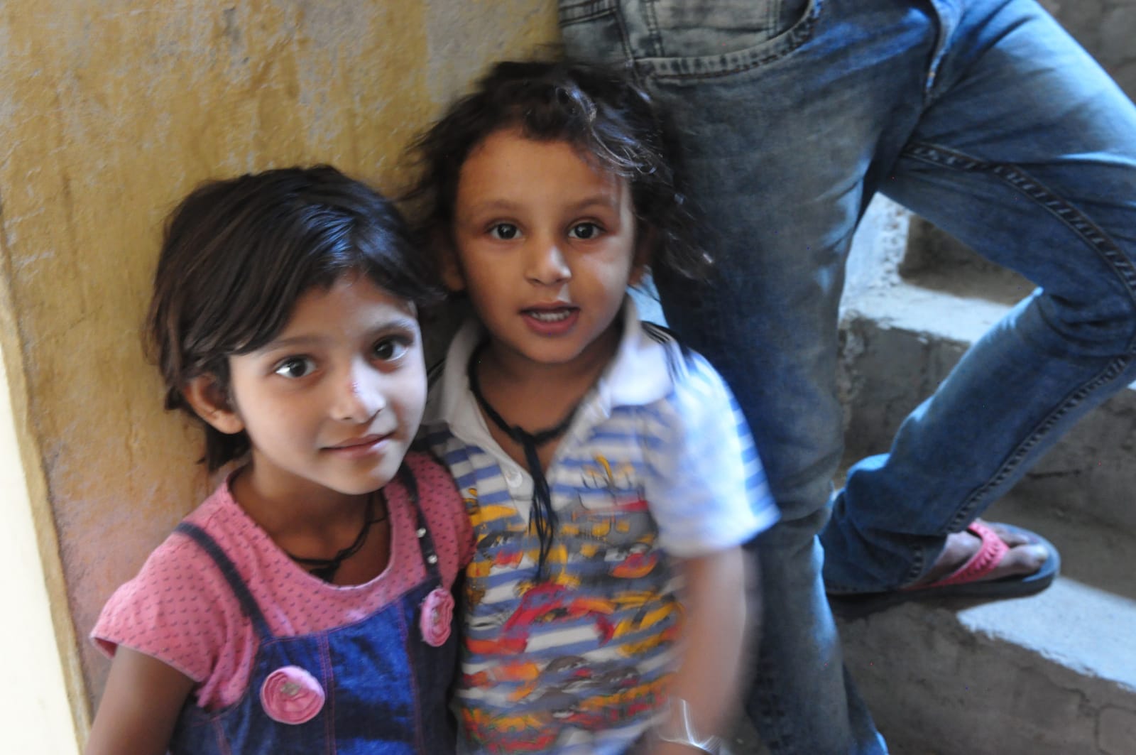 Two children standing close together inside Baba’s home.