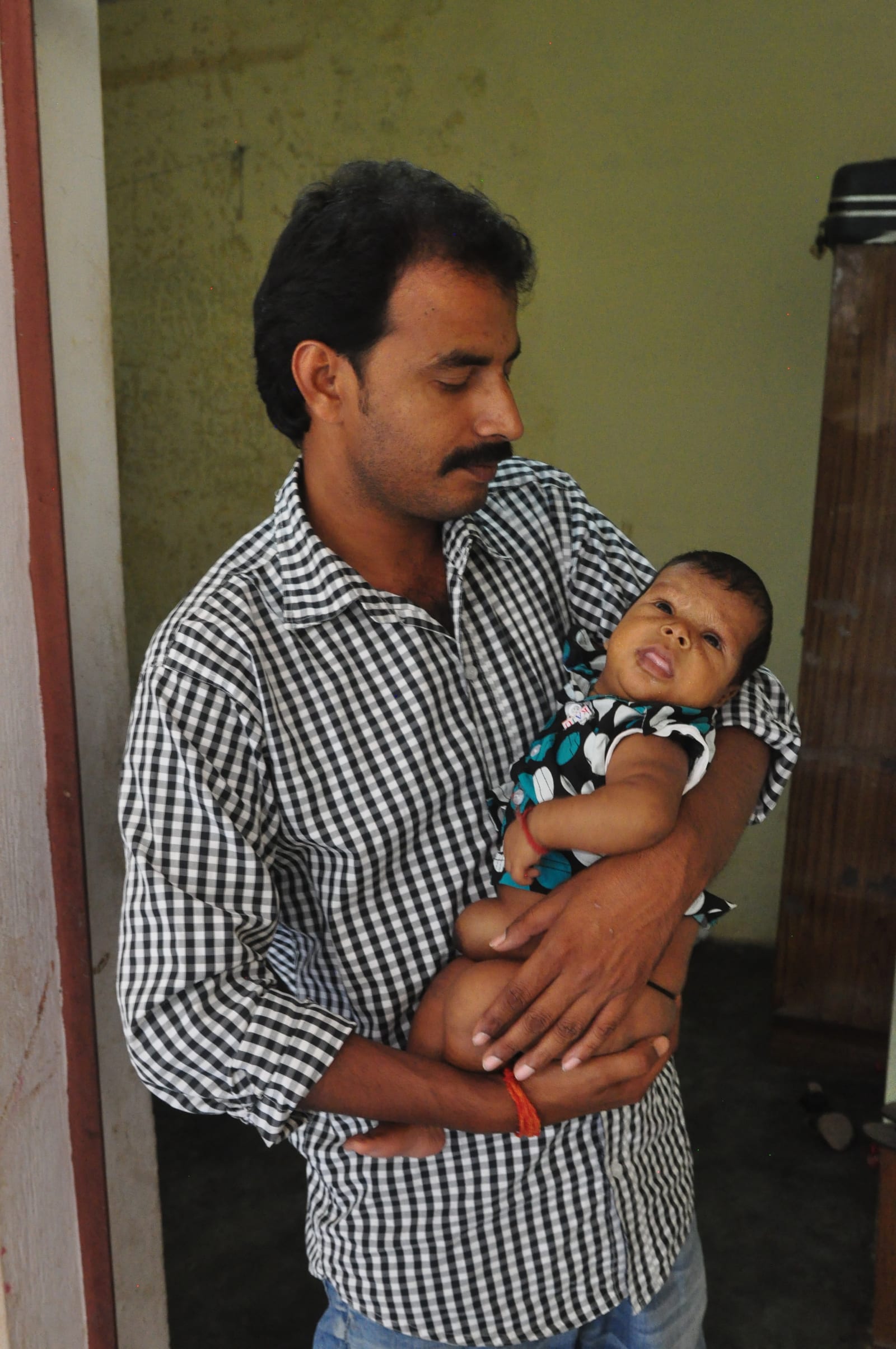 Baba in a checked shirt holding his child in a doorway.