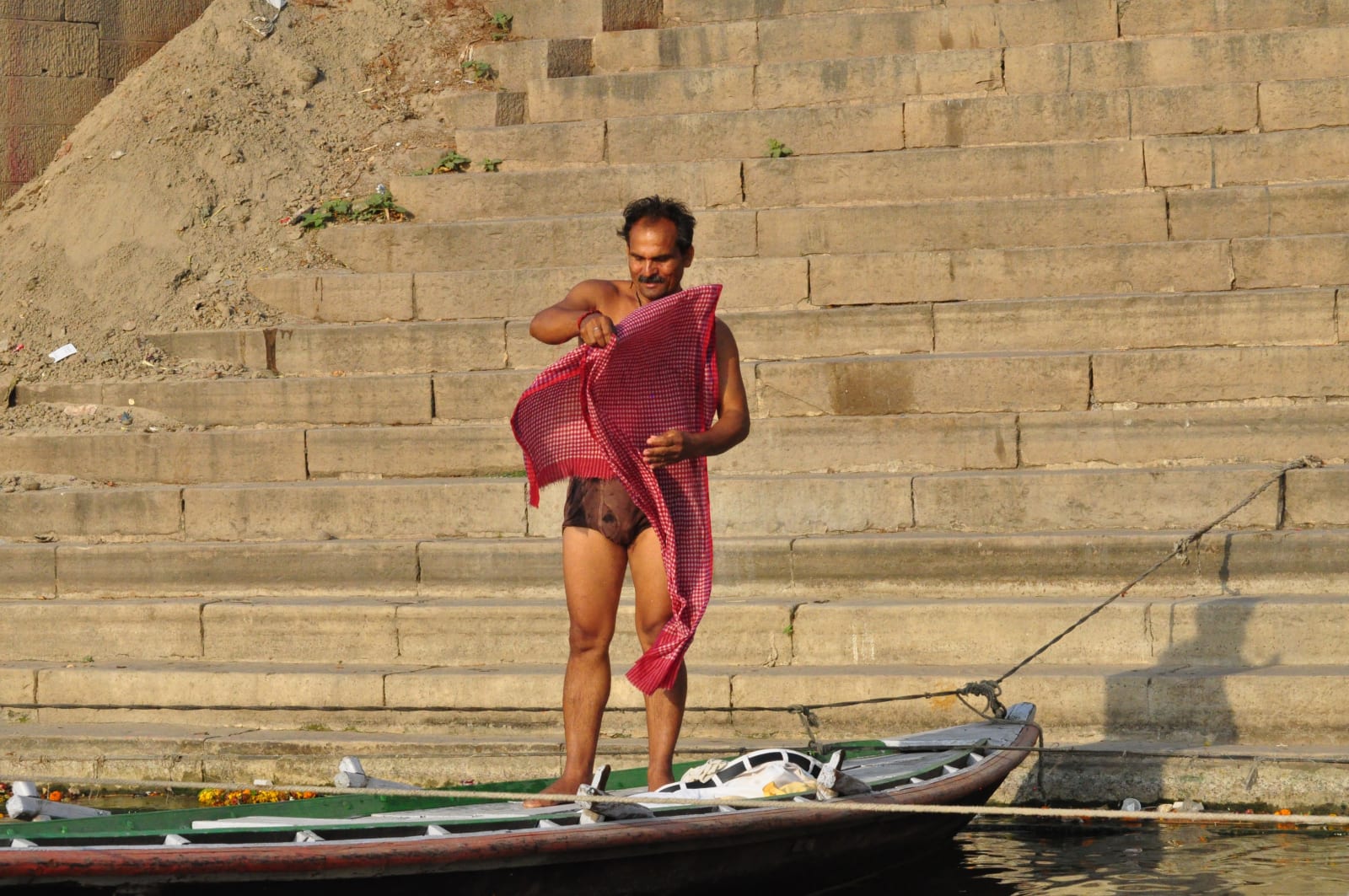 Pandu holding out the red checked cloth at the edge of the river.