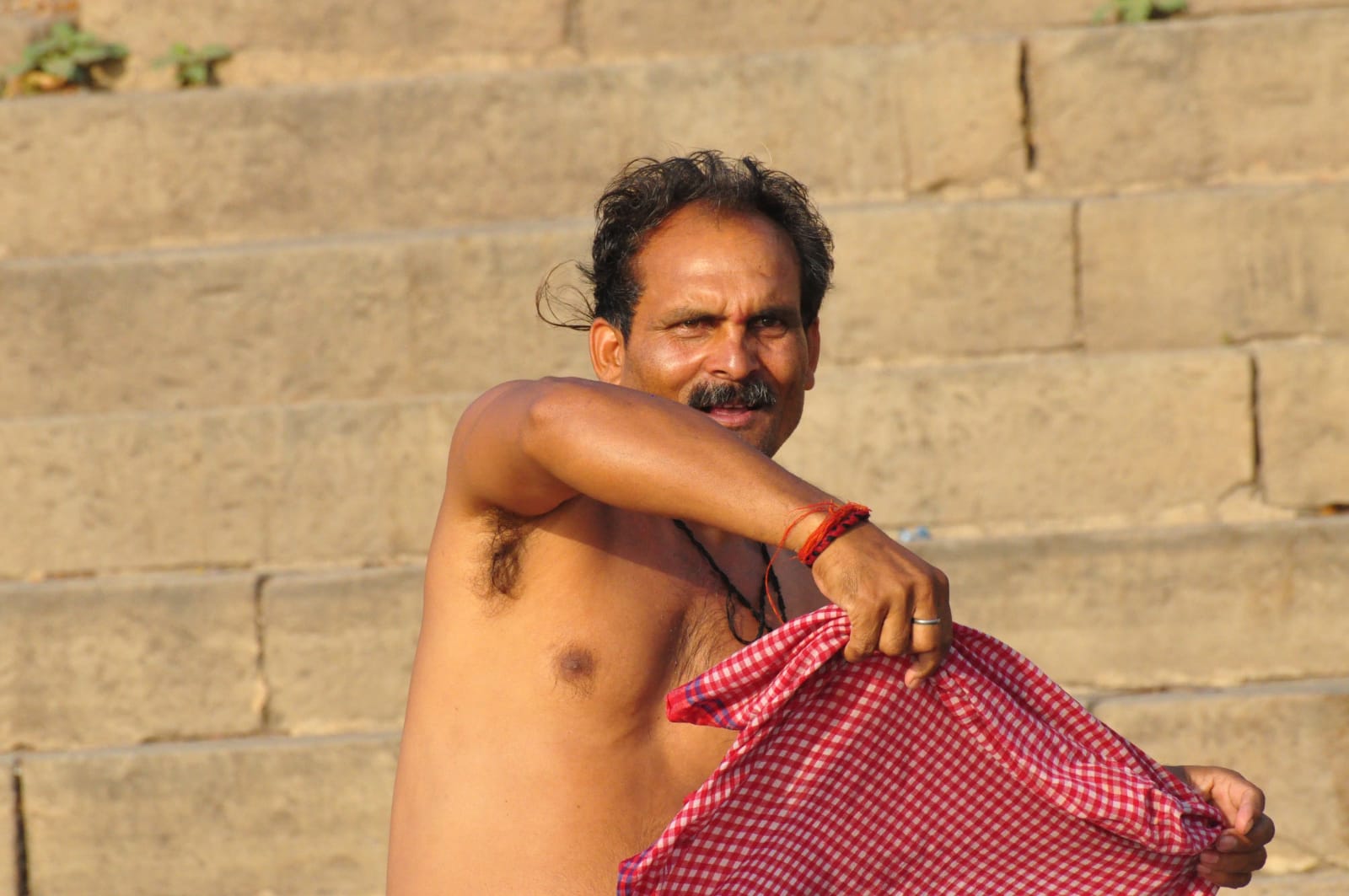 A closer view of Pandu holding the cloth, with the ghat steps behind him.